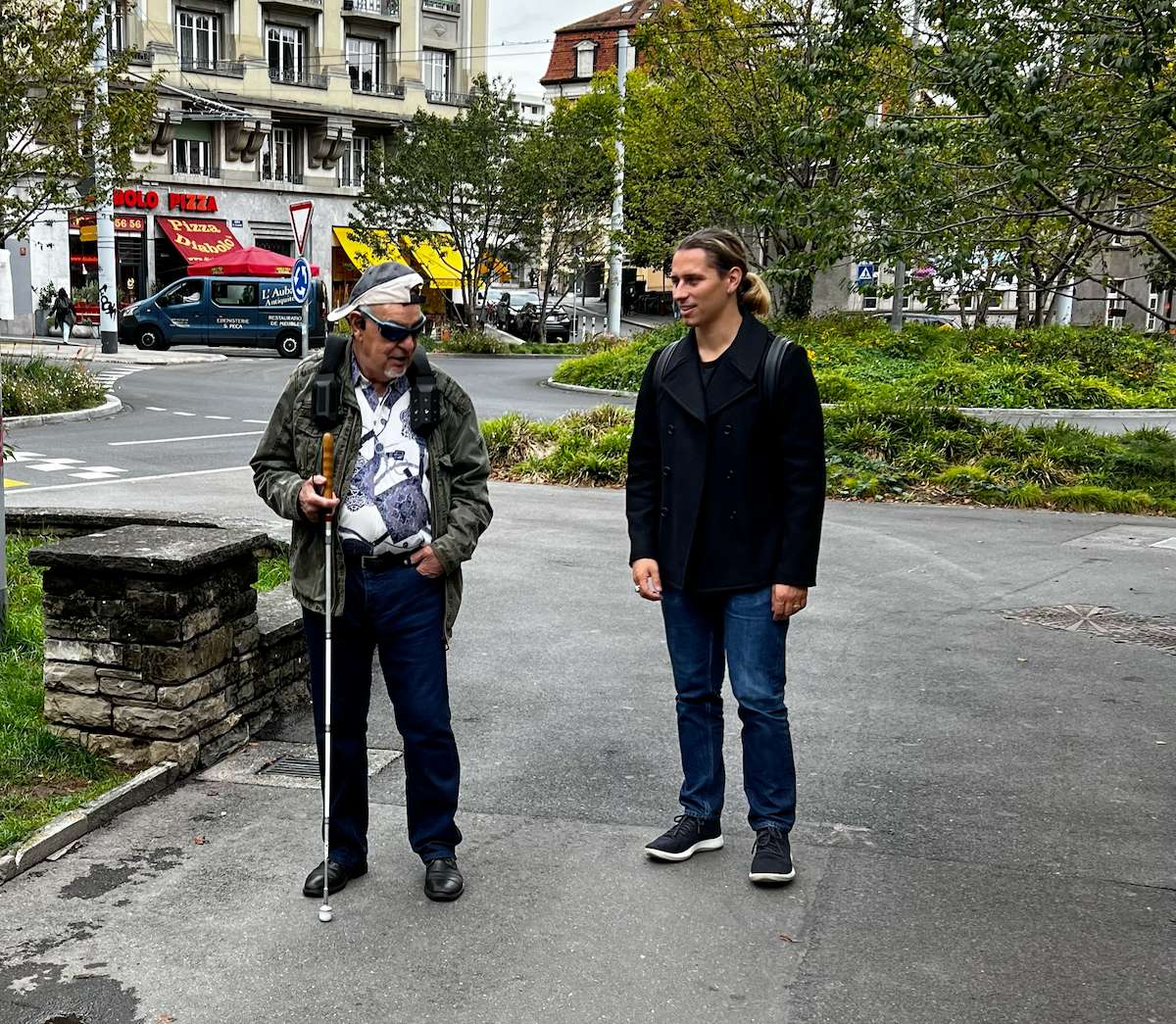 A person walking with a NOA user, in the street, likely providing a mobility training session.