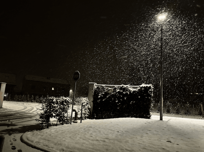 A picture in a low light setting in the street under a snowfall.